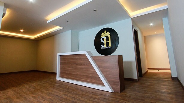 A hotel reception area with a modern design, featuring a reception desk, a logo on the wall, and recessed lighting. - TriDD 01 Sriwijaya Hotel (Mataram)