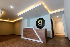 Un espace d’accueil d’hôtel au design moderne, comprenant un comptoir de réception, un logo sur le mur et un éclairage encastré.
