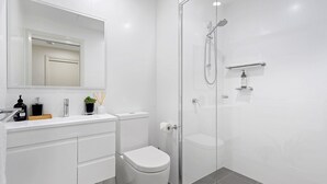 Un baño moderno con cabina de ducha de vidrio, inodoro blanco y tocador con artículos de aseo.