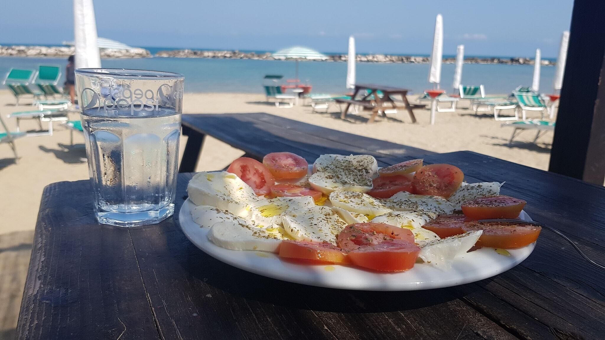 A plate of Caprese salad with tomatoes and mozzarella on a wooden table at a beach.