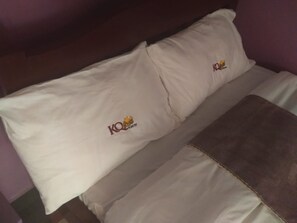A bed with two pillows, each featuring a logo and text. - KQ Grill and Bistro (Eldoret)