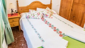 A bedroom with a wooden bed, floral bedding, a green towel, and two pink wall art pieces.