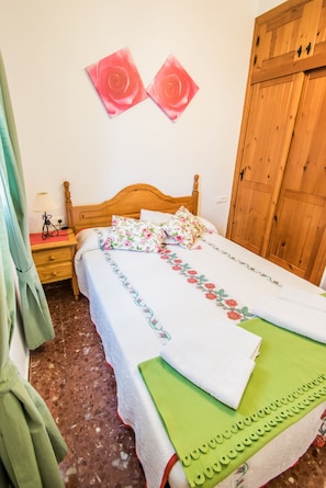 Une chambre avec un lit en bois, une literie à motifs floraux, une serviette verte et deux œuvres d’art roses accrochées au mur.