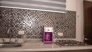 A kitchen with a tiled backsplash, a purple coffee maker, a gas stove, and a sink. - Hot tub 1 bedroom AC Security 2 blocks from lleras (Medellin)