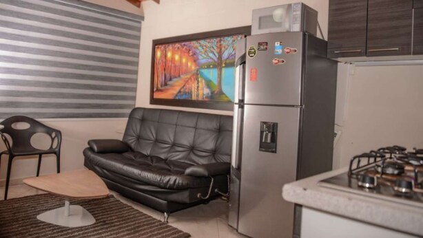 A compact living space with a black leather sofa, a refrigerator, a gas stove, and a painting on the wall. - Hot tub 1 bedroom AC Security 2 blocks from lleras (Medellin)