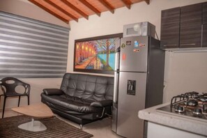 Un espace de vie compact comprenant un canapé en cuir noir, un réfrigérateur, une cuisinière à gaz et un tableau accroché au mur.