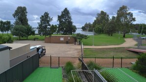 Vista de un parque con un lago, un edificio de ladrillo y un área cercada con césped artificial verde.