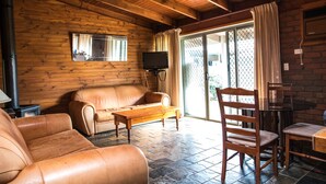 A cozy cabin interior with a wooden ceiling, a leather sofa, a wooden table, and a chair. - Water's Edge Bundalong (Bundalong)