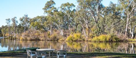 A lakeside picnic area with a table and chairs, surrounded by trees and a calm body of water.