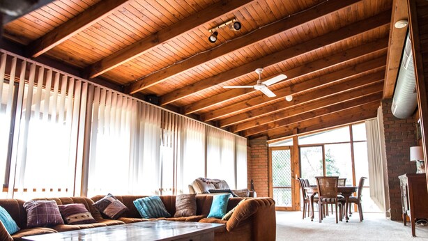 A spacious room with a high ceiling, wooden beams, a large window, a sofa, a dining table with chairs, and a ceiling fan. - Water's Edge Bundalong (Bundalong)