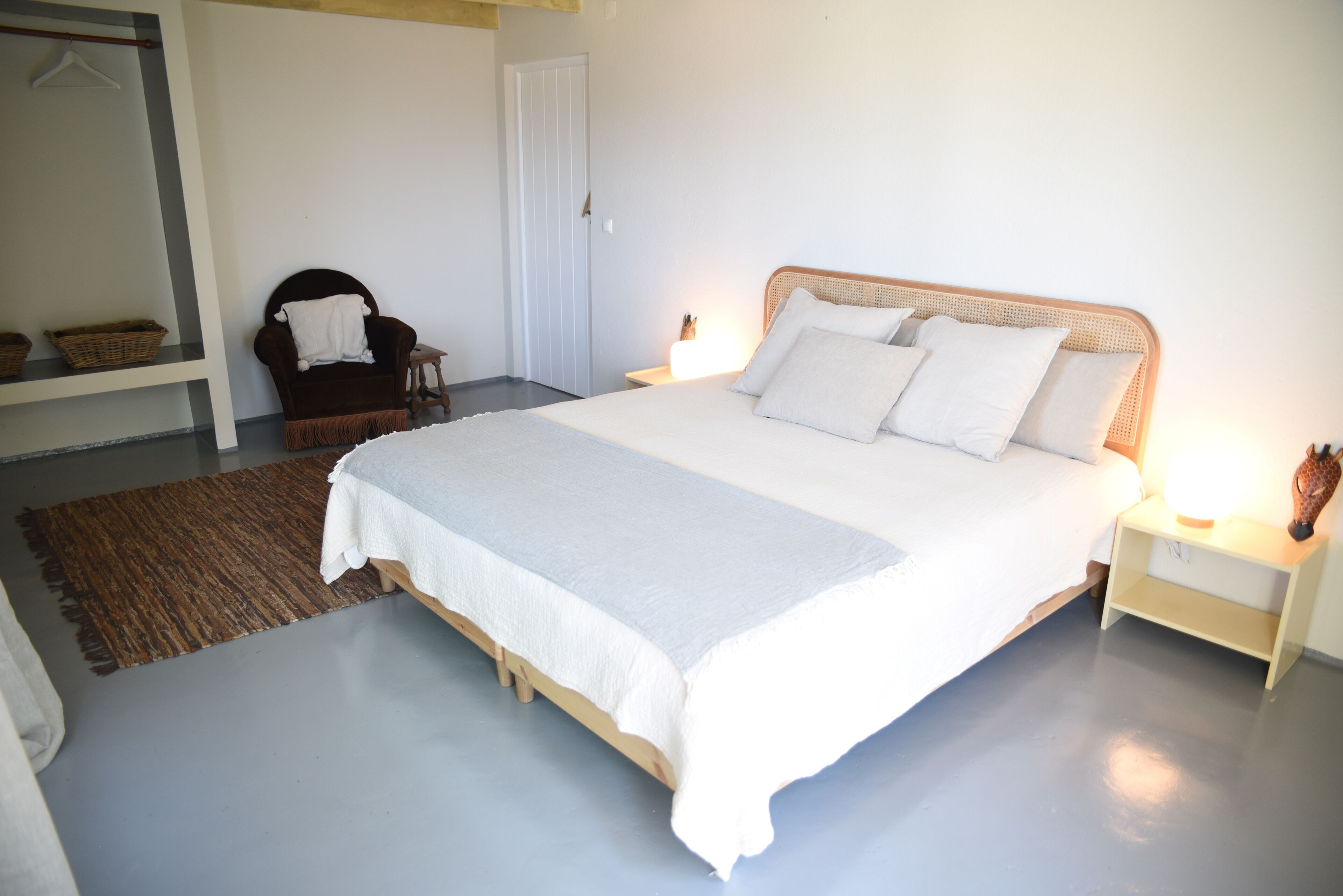 A bedroom with a large bed, a chair, a nightstand, and a wardrobe.