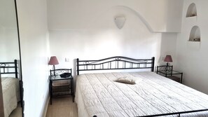 Een slaapkamer met een bed, twee nachtkastjes met lampen, een stoel en een klein tafeltje met een mand.