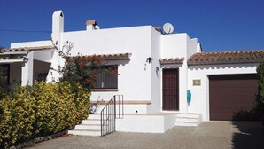 A white building with a brown door, a satellite dish, and a small window with red flowers.