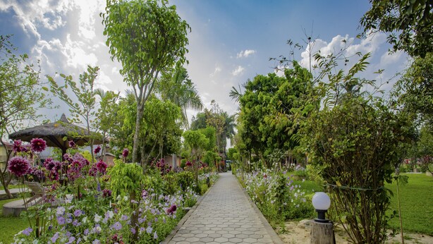 Ein gepflasterter Gartenweg, gesäumt von blühenden Pflanzen und Bäumen, der zu einem Gazebo führt.