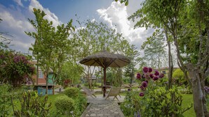 Ein Gartenweg führt zu einem Gazebo mit einem Reetdach und Sitzgelegenheiten.