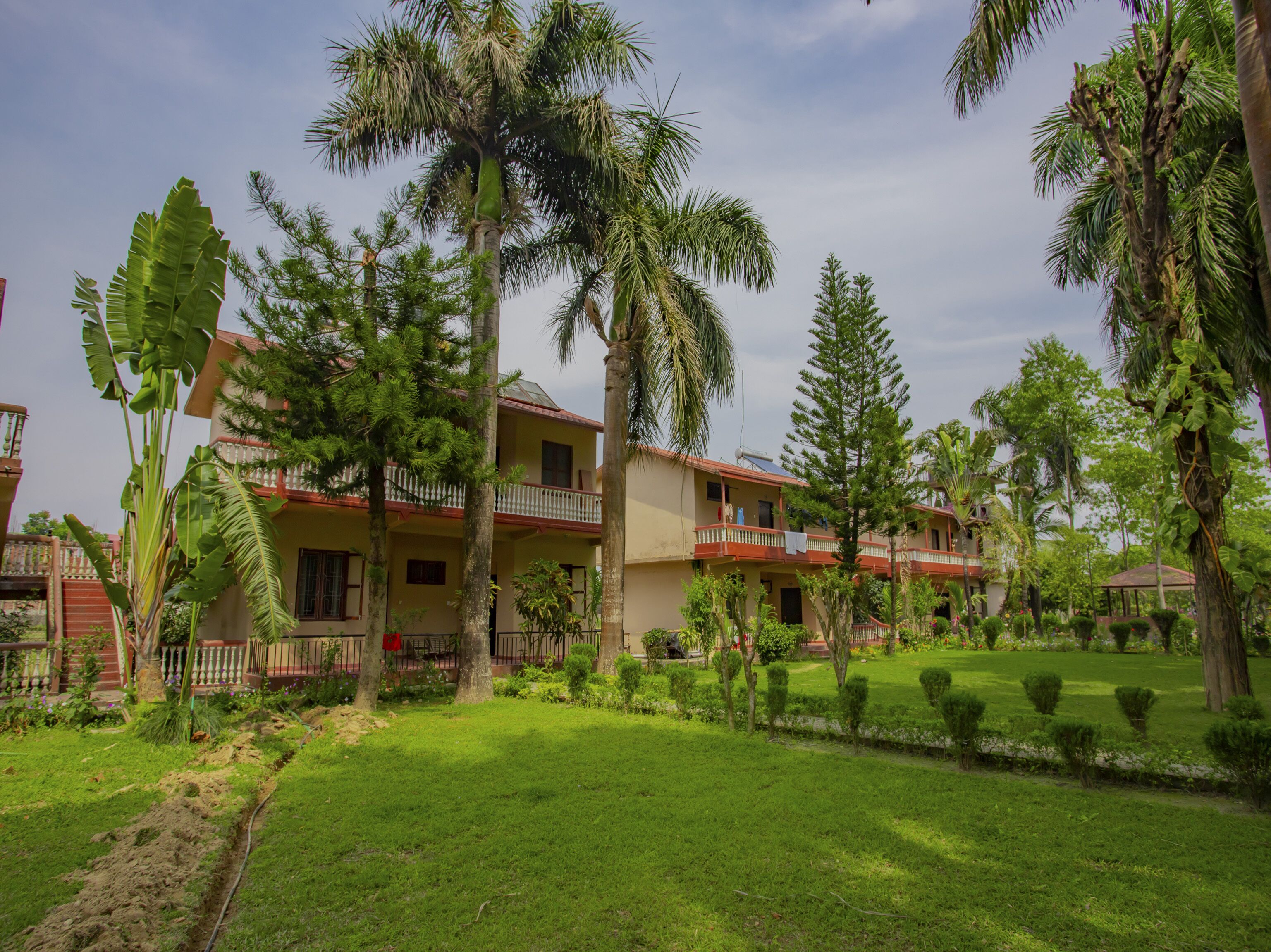 A two-story building with a balcony, surrounded by lush greenery and palm trees.