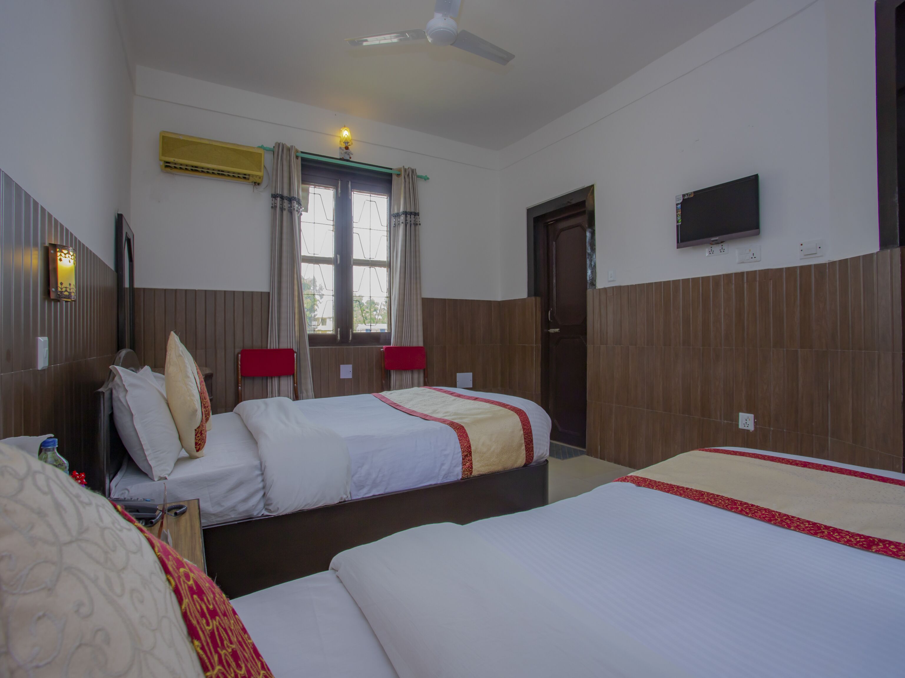 Habitación de hotel con dos camas, un televisor en la pared y una ventana con cortinas.