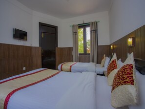 Habitación de hotel con dos camas, un televisor montado en la pared, una puerta y una ventana con cortinas.