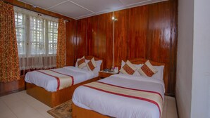Ein Hotelzimmer mit zwei hölzernen Betten, einem großen Fenster mit Vorhängen und einem Fliesenboden.
