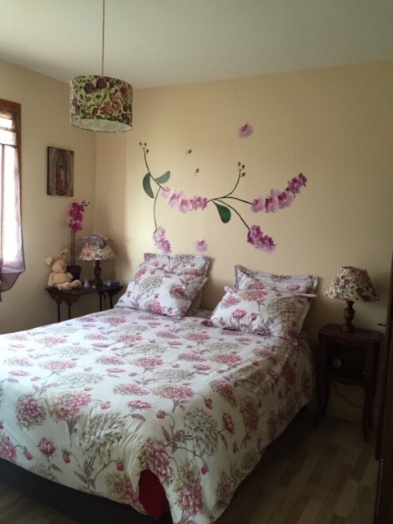 Un dormitorio con una colcha estampada de flores, una lámpara de pared y una mesita de noche pequeña.