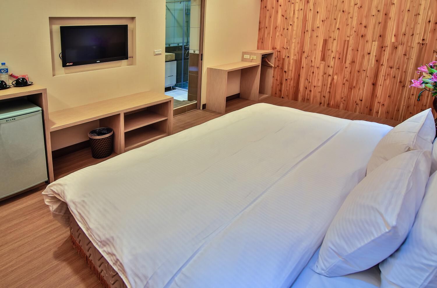 Une chambre d’hôtel avec un grand lit, un téléviseur fixé au mur, un bureau en bois et une armoire en bois.