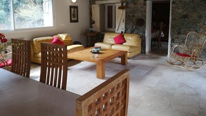 Una sala de estar acogedora con pared de piedra, sofá amarillo, muebles de madera y vistas al exterior.