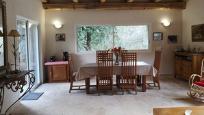 Un comedor con mesa y sillas de madera, ventana con vistas a la vegetación y pared de piedra.