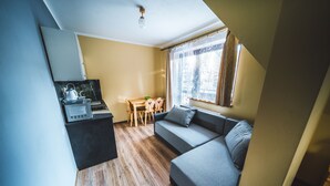 A compact living space with a kitchenette, a sofa, a dining table, and a window with curtains. - Pokoje i Apartamenty Nad Potokiem (Zakopane)