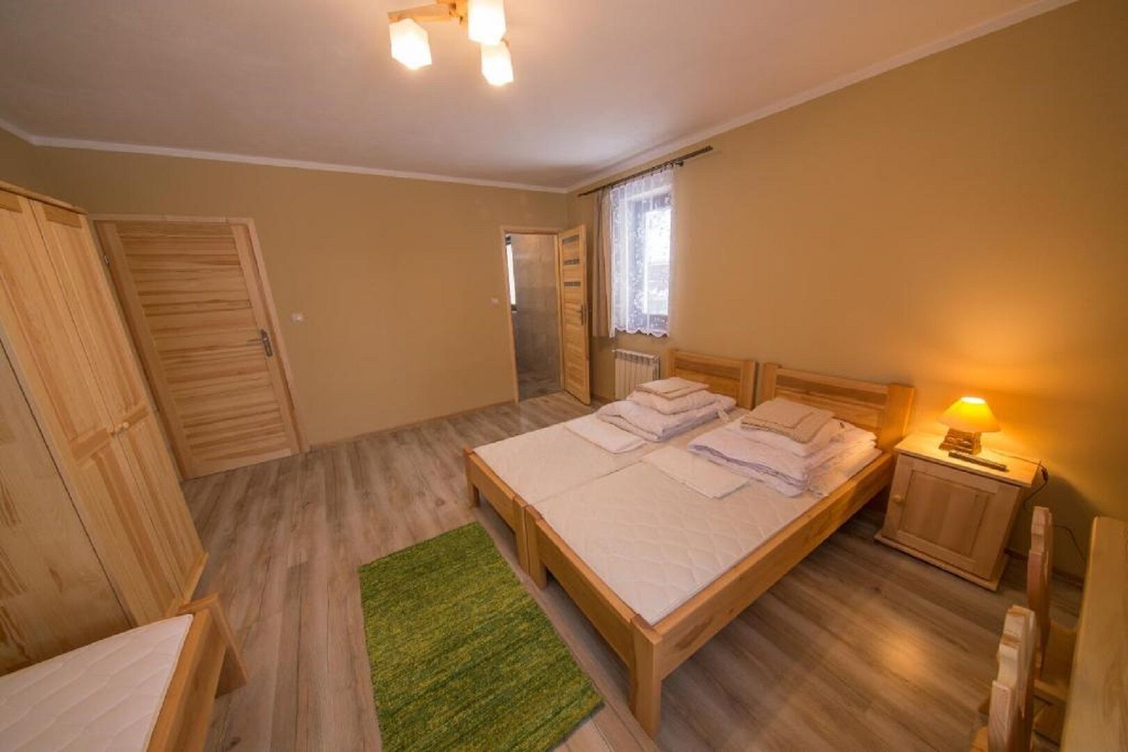 A bedroom with a large bed, two bedside tables, a green rug, and wooden flooring.