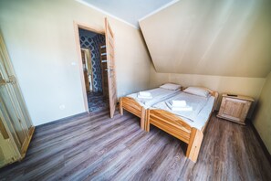 A bedroom with a sloped ceiling, wooden flooring, a bed with a wooden frame, and a small wooden nightstand. - Pokoje i Apartamenty Nad Potokiem (Zakopane)