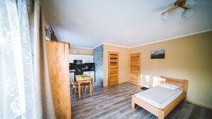 A bedroom with a wooden bed, a dining table with chairs, a kitchen in the background, and a wardrobe. - Pokoje i Apartamenty Nad Potokiem (Zakopane)