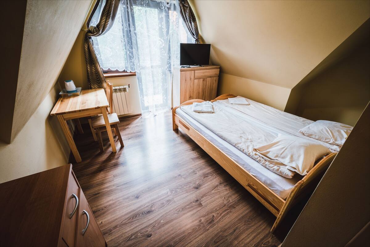 A small, cozy room with a bed, a desk, a chair, and a TV on a wooden cabinet.