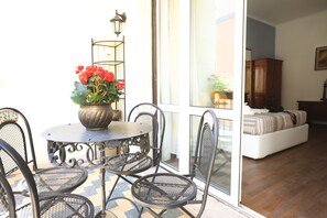 A dining area with a round table and four chairs, a potted plant with red flowers, and a view of a living room through a glass door. - Unique Luxury Apartment and Rooms (Rome)