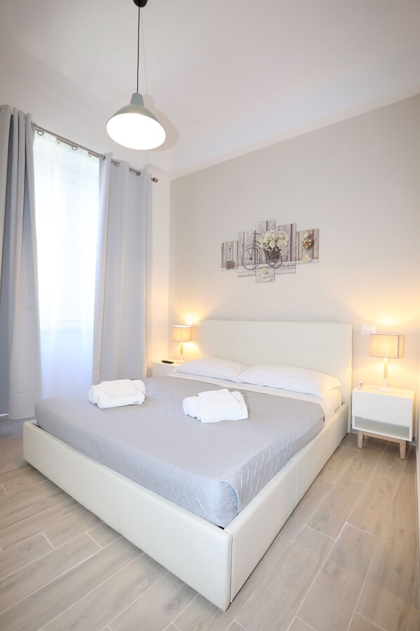 A modern bedroom with a large bed, two bedside tables with lamps, a hanging light fixture, and a wall art piece. - Unique Luxury Apartment and Rooms (Rome)