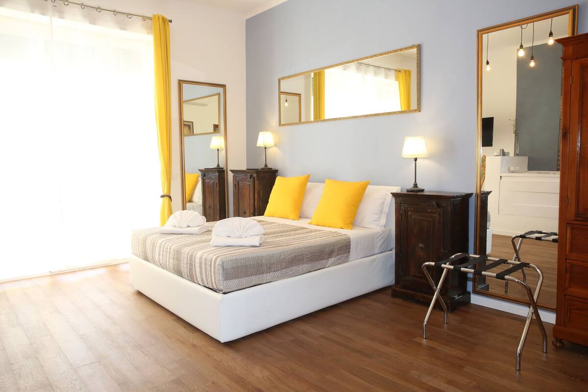 Une chambre à coucher avec un grand lit, deux tables de chevet avec des lampes, une armoire en bois et un miroir au mur.