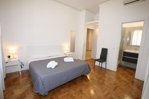 A modern bedroom with a large bed, bedside tables, a chair, and a bathroom visible through an open door. - Unique Luxury Apartment and Rooms (Rome)