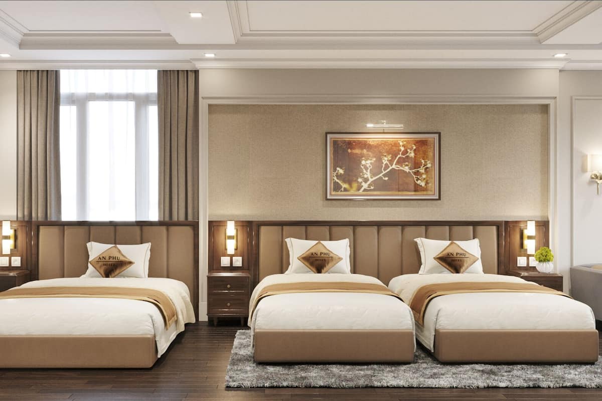 A hotel room with three beds, a large window with curtains, a framed artwork above the beds, and a logo on the wall.