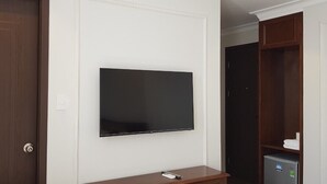 Quarto com televisão de tela plana fixada na parede, um armário de madeira e uma geladeira pequena.