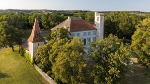 A historic building with a prominent tower and a large central structure, surrounded by lush greenery and a stone wall. - Chateau les Estournels (Lendou-en-Quercy)