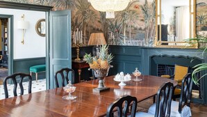 A dining room with a wooden table, chairs, a chandelier, a candelabra, and a mural of tropical scenery. - Chateau les Estournels (Lendou-en-Quercy)