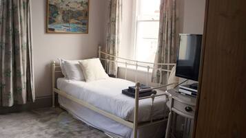 A bedroom with a single bed, a painting on the wall, a window with curtains, and a television on a stand.