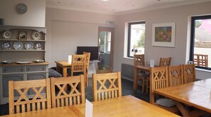 A dining area with wooden tables and chairs, a television, and a wall-mounted clock. - The Globe Angle (Pembroke)