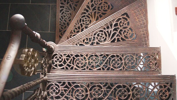 Eine Treppe mit aufwendiger Metallgeländerung und einem hölzernen Handlauf.