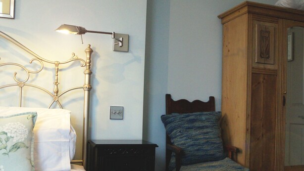 Un dormitorio con cama, mesita de noche, silla de madera y armario.