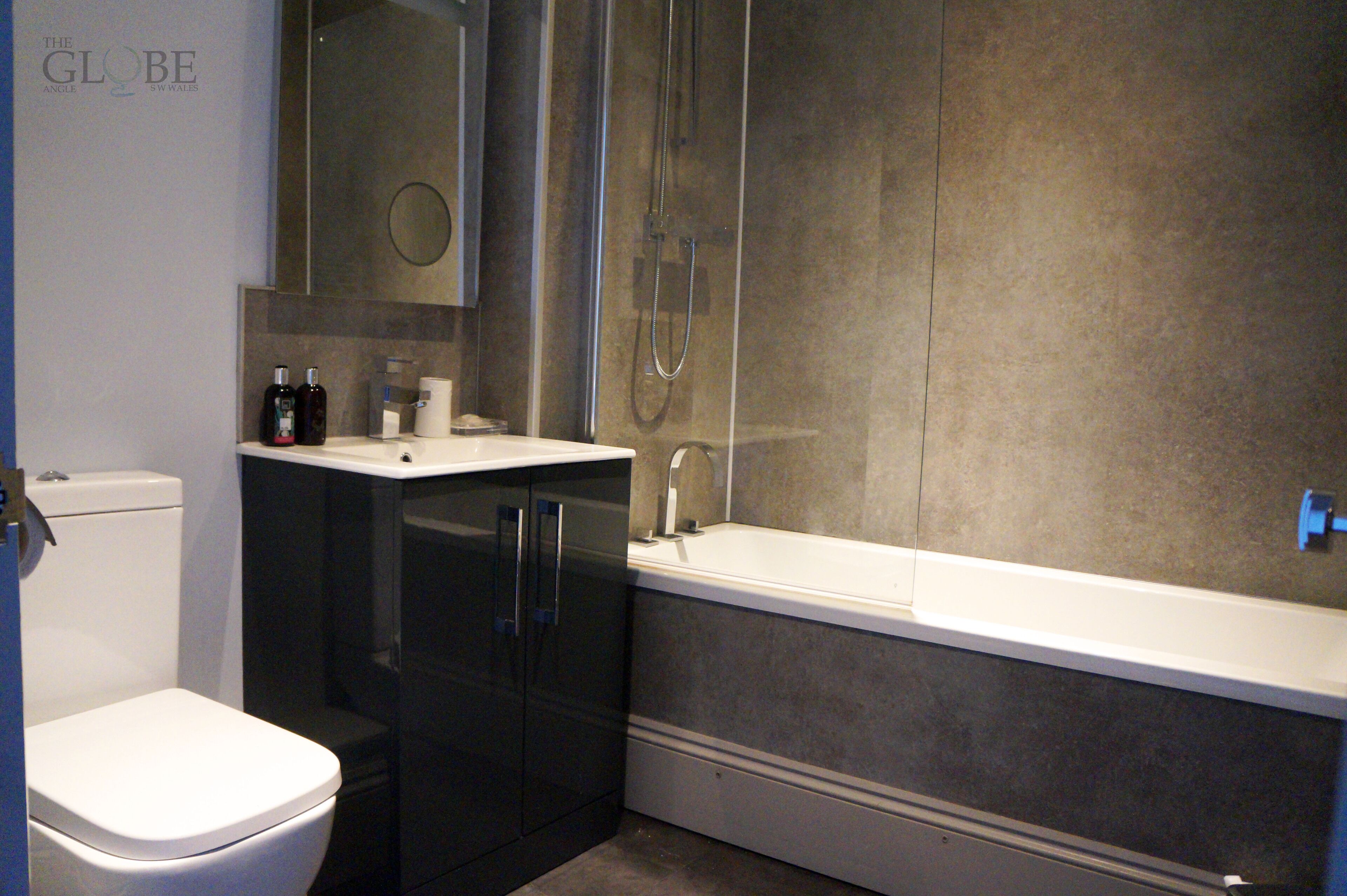 Un baño moderno con inodoro, armarios oscuros, lavamanos y bañera.