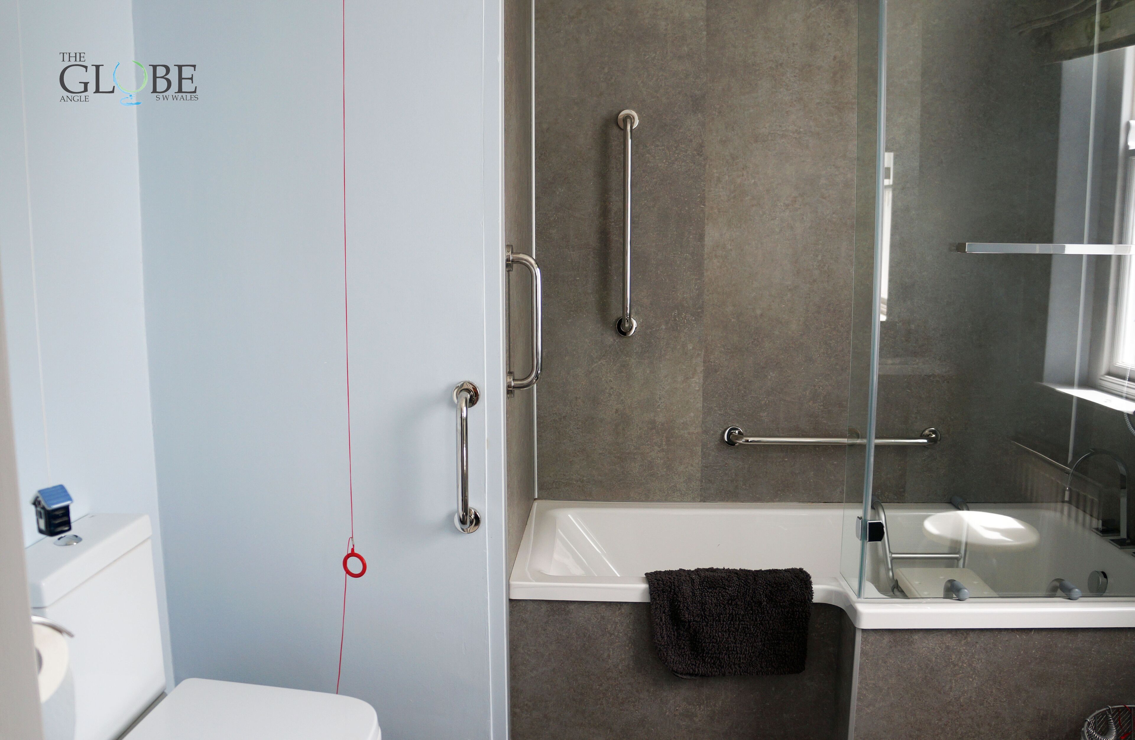 Et badeværelse med et hvidt toilet, en brusekabine med glasdør og et spejl over vasken.