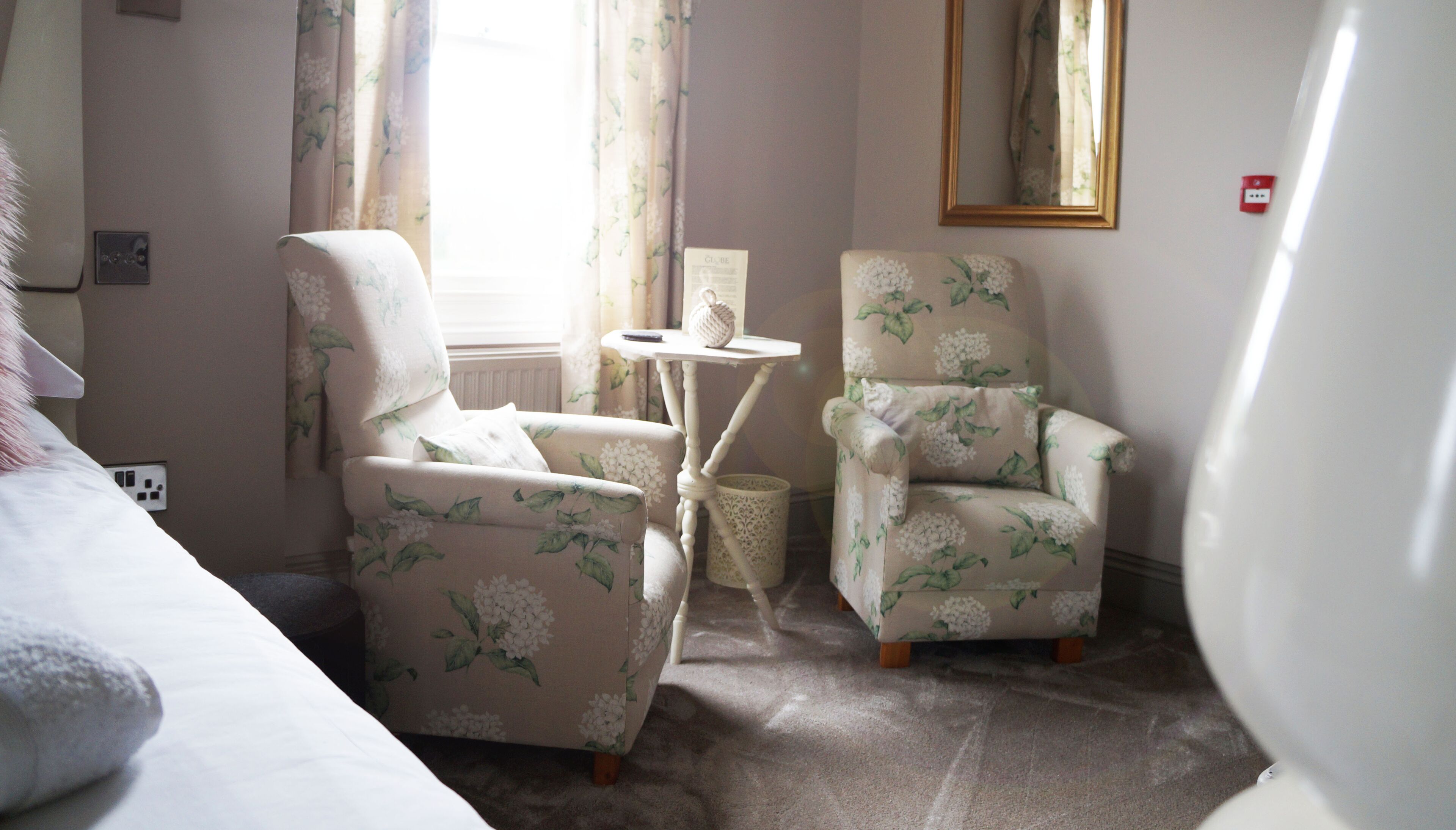 A cozy room with two floral-patterned armchairs, a small white table, and a window with curtains.