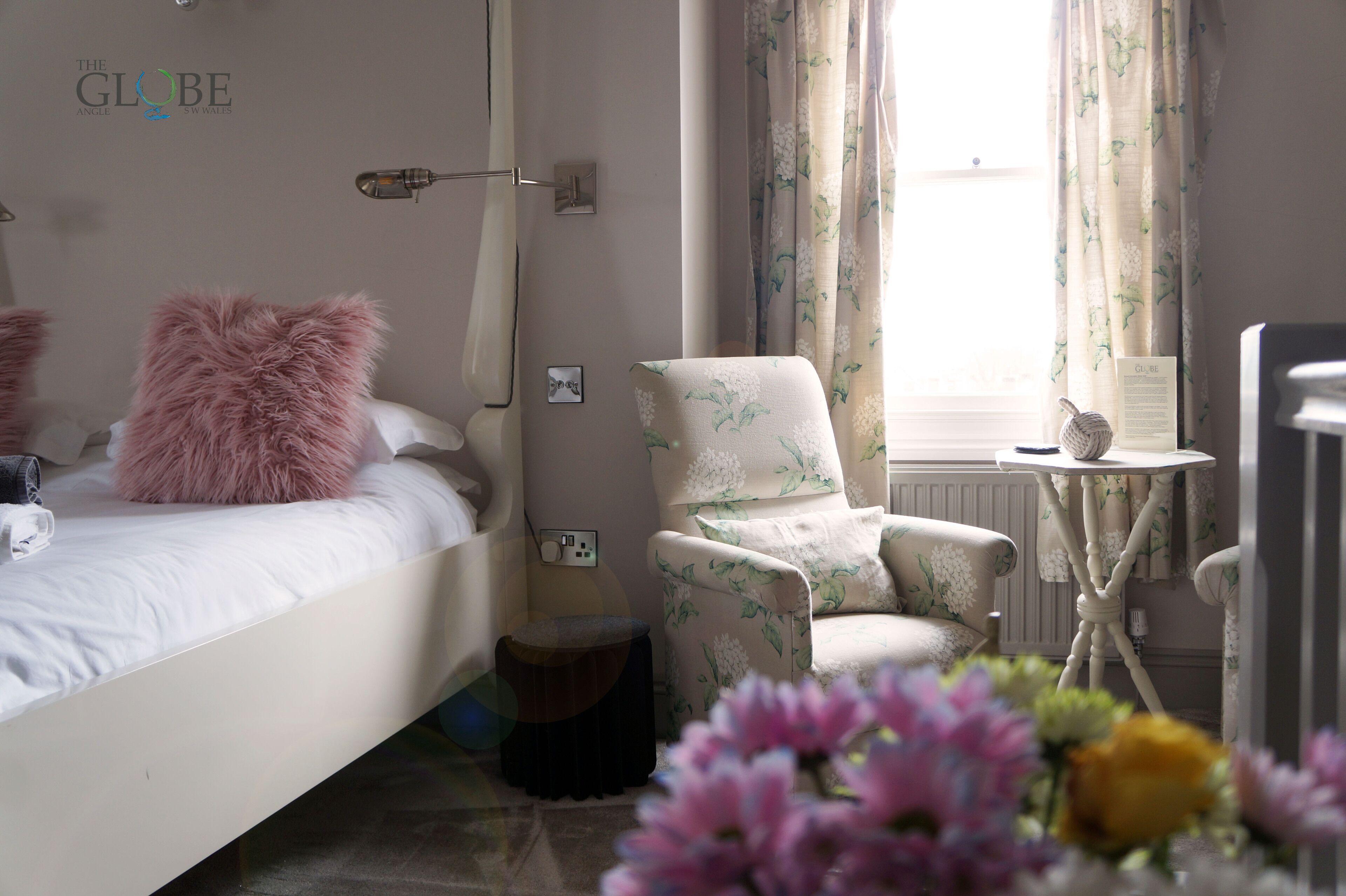 A bedroom with a bed, a chair, a small table, and a window with curtains.