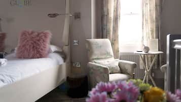 A bedroom with a bed, a chair, a small table, and a window with curtains.