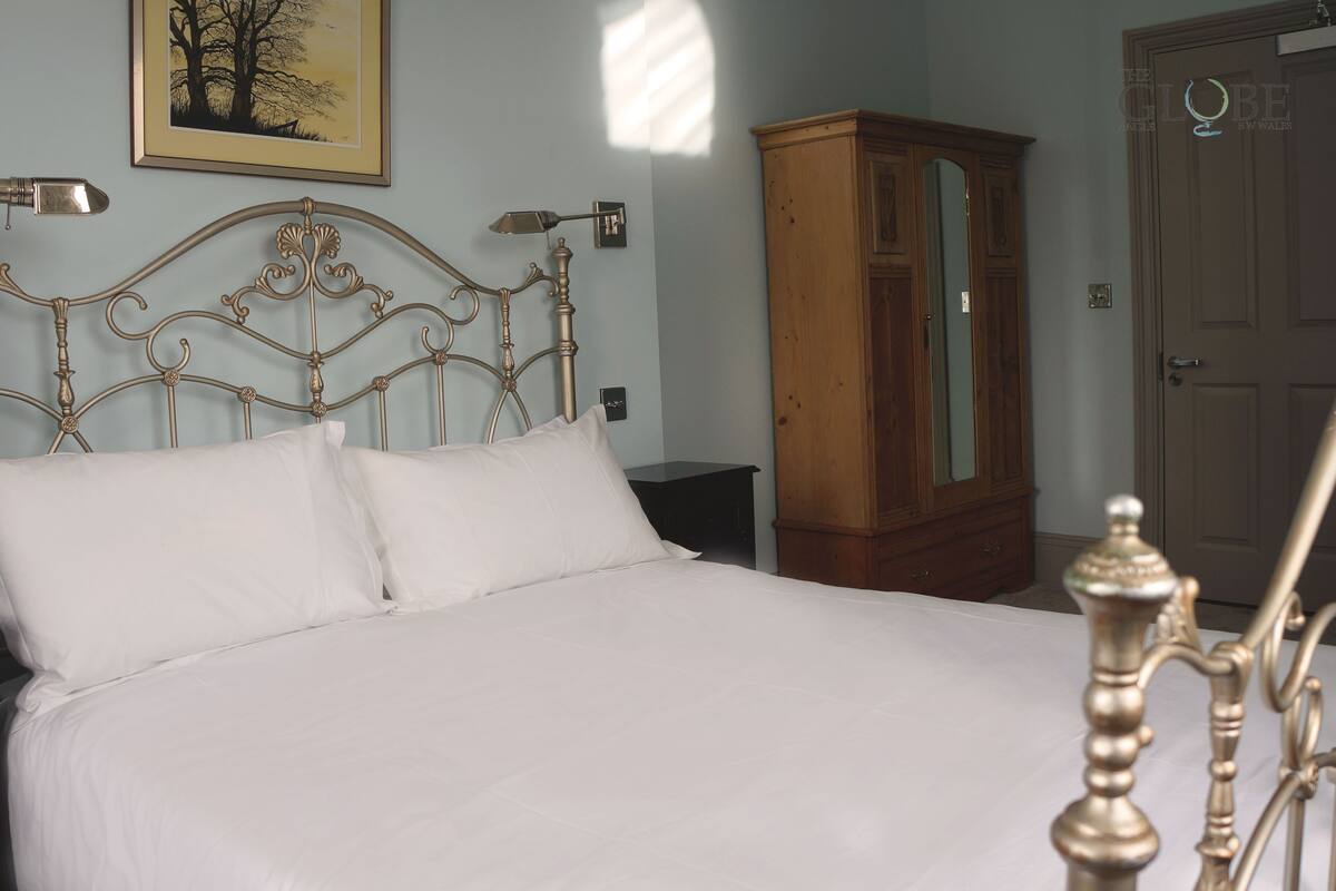 A bedroom with a metal-framed bed, a wooden wardrobe, and a framed picture on the wall.